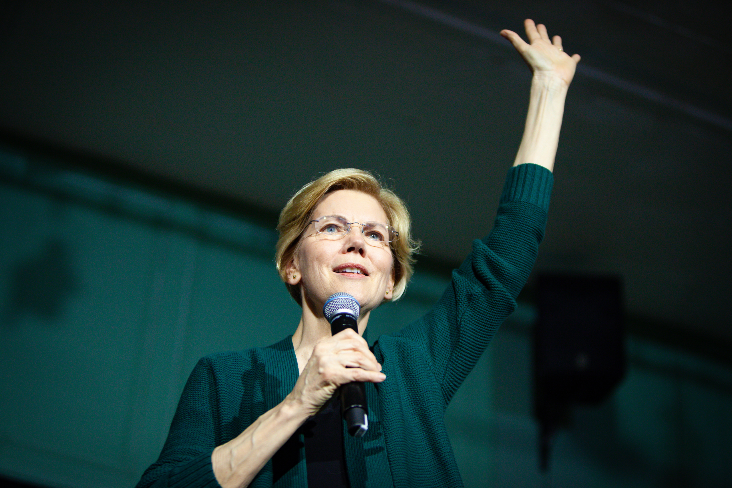 Elizabeth Warren with microphone in hand and other hand raised