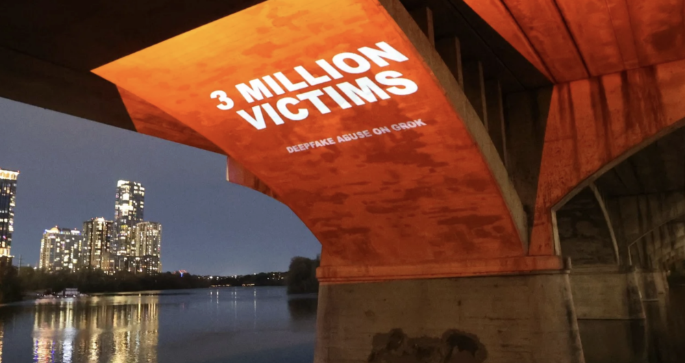A nighttime view of a city skyline reflected on water, with a large concrete bridge in the foreground lit in orange. Projected onto the underside of the bridge are the words “3 MILLION VICTIMS” and “DEEPFAKE ABUSE ON GROK.”